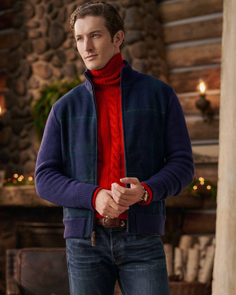 Man wearing a red cable knit turtleneck jumper, navy jacket and jeans.
